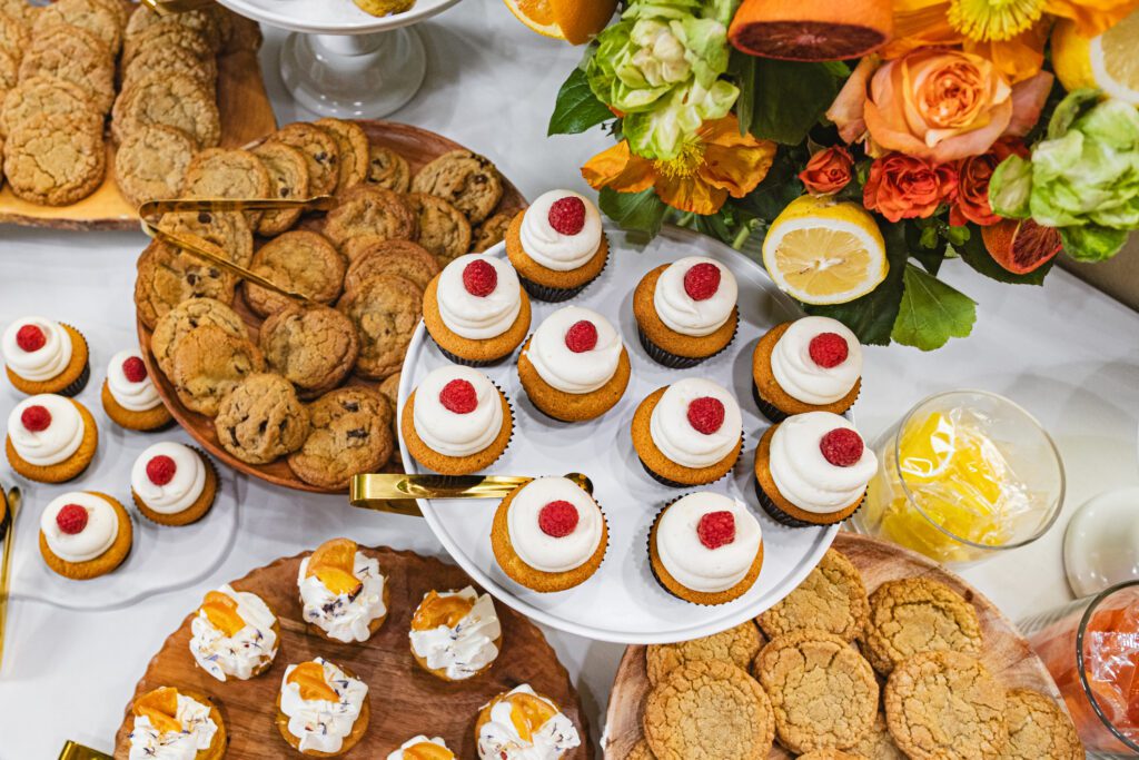 A variety of cookies and cupcakes arranged on plates with roses in the background.