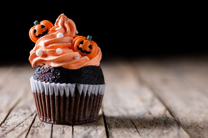 Chocolate cupcake with orange Halloween frosting and pumpkin decorations.