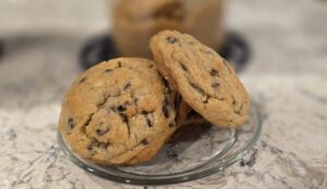 Two chocolate chip cookies on a clear glass plate.