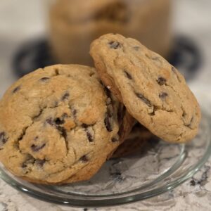 Two chocolate chip cookies on a clear glass plate.
