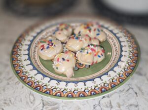 Decorated cookies with white icing and colorful sprinkles on a patterned plate.