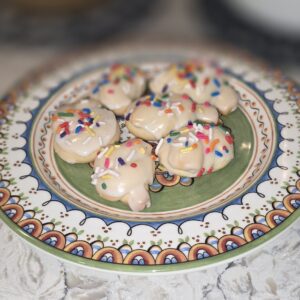 Decorated cookies with white icing and colorful sprinkles on a patterned plate.