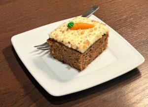 A square piece of carrot cake with cream cheese frosting on a white plate.