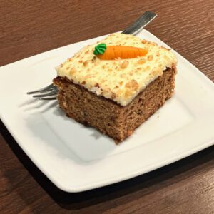 A square piece of carrot cake with cream cheese frosting on a white plate.