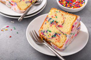 Slice of colorful funfetti cake with icing on a plate.