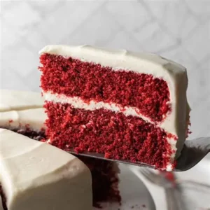 A slice of red velvet cake with white frosting on a plate.