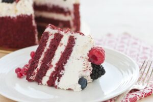 Slice of red velvet cake with cream cheese frosting and berries.
