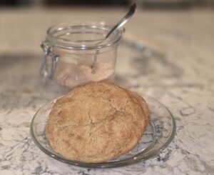 A round loaf of bread on a glass plate with a spoon and jar in the background.