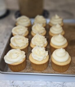 Tray of cupcakes with creamy white frosting in a bakery.
