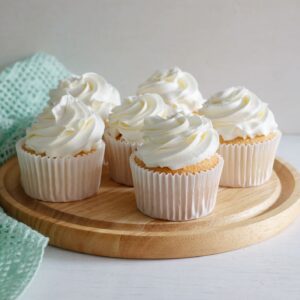 Four vanilla cupcakes with swirled white frosting on a wooden tray.