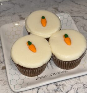 Three carrot cake cupcakes with white frosting and carrot decorations.
