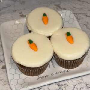 Three carrot cake cupcakes with white frosting and carrot decorations.