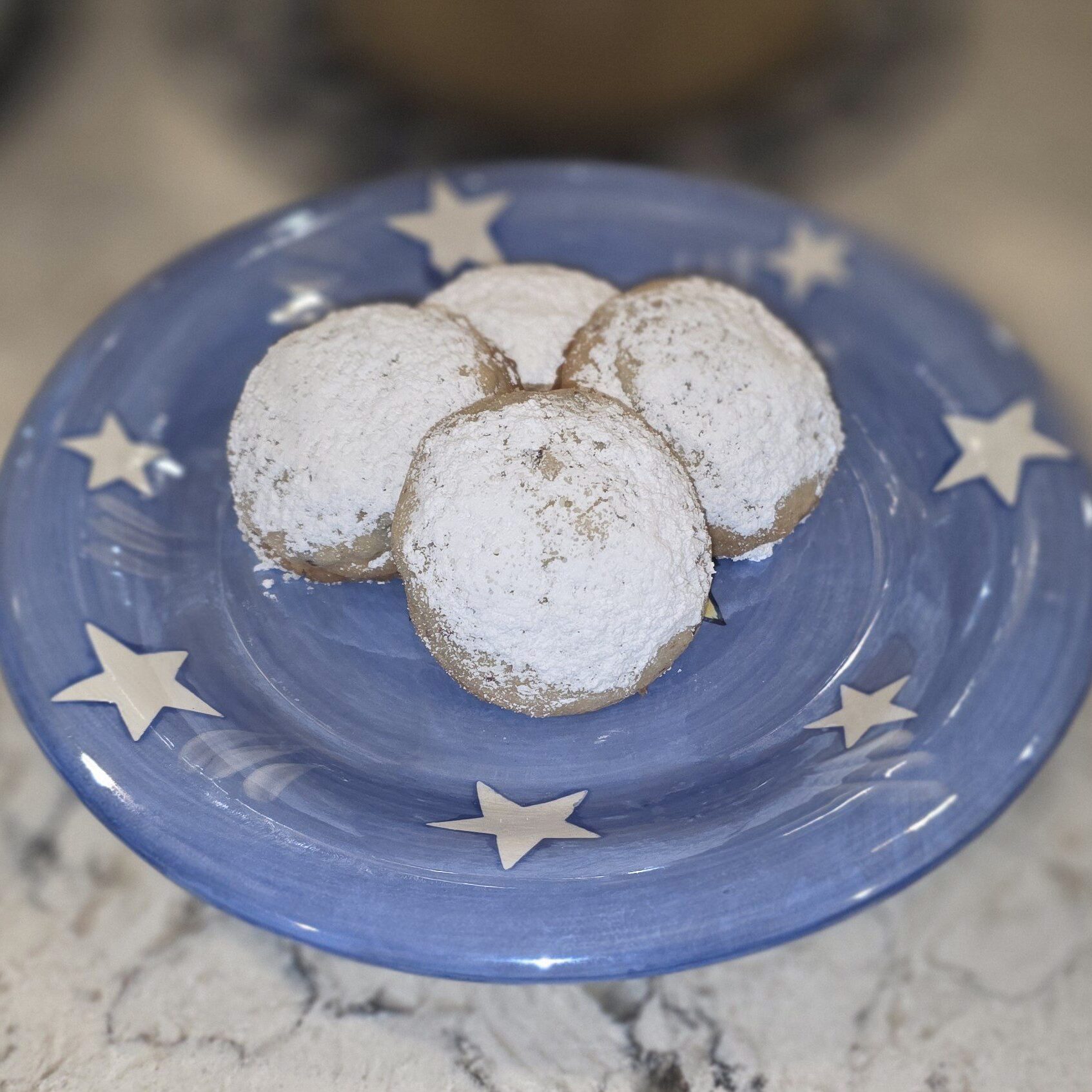 Three powdered sugar-coated cookies on a blue star-patterned plate.